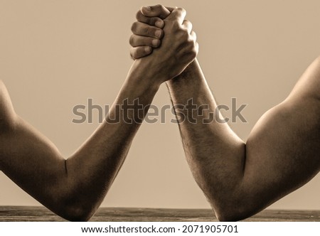 Arm wrestling. Heavily muscled man arm wrestling a puny weak man. Arms wrestling thin hand and a big strong arm in studio. Two man's hands clasped arm wrestling, strong and weak, unequal match.
