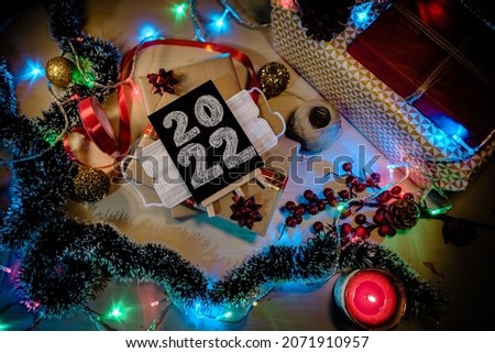 Christmas flat lay 2022 with covid face mask. Aerial picture with candles, presents, christmas light, chalkboard or ribbon. Concept: happy new year