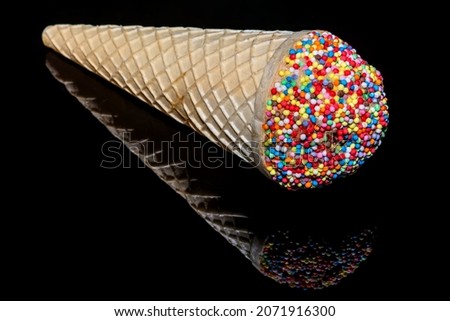 Ice cream cone with little cup cake decorated with frosting and round sprinkles with sprinkles scattered 