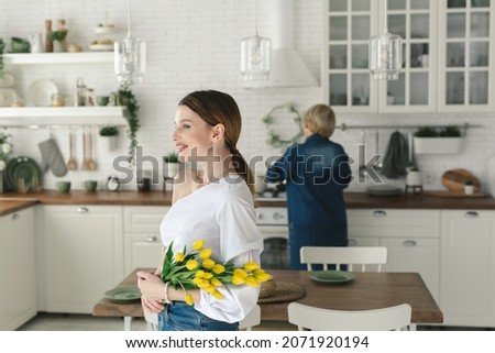 Beautiful girl stands in the kitchen and holds tulips in her hands. Women's day March 8