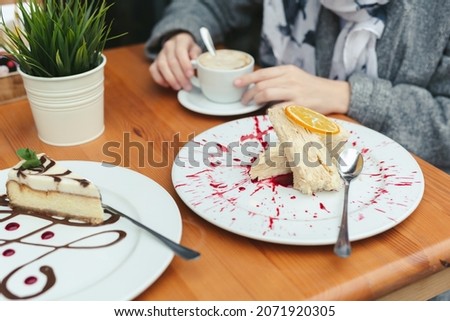 Close-up of a cake in a cafe. Adult mother and daughter at the table, drinking coffee and eating cakes. Attention is focused on the cake and hands.