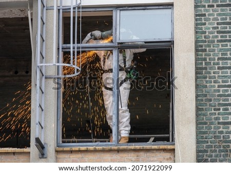 Worker with white protective suit, gloves and mask removes removal white asbestos on construction site. Demolition building. Action picture. Asbestosis, hazard, part of a serie.  