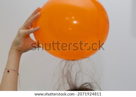 A child raises their hair whilst exploring static electricity with an inflated orange balloon. Royalty-Free Stock Photo #2071924811