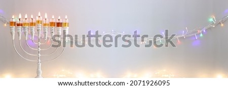 Image of jewish holiday Hanukkah with menorah (traditional candelabra) and oil candles over garland glitter lights background