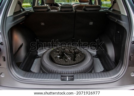 Spare wheel in the trunk of a modern car. Jack lifting and a spare tire in rear of car. Royalty-Free Stock Photo #2071926977