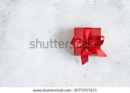 Red gift box with a red satin ribbon (bow) on a light background. Congratulatory concept for Valentine's Day, Christmas, New Year, Birthday, top view,copy space