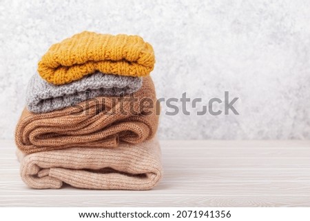 Pile of warm knitted clothes, sweaters and caps on rustic white wooden background. Cozy folded knitwear stack, winter wardrobe capsule concept, shopping, free space for text