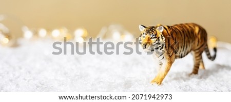 Figurine of tiger in snow on beige background. Tiger symbol of the Chinese new year 2022. Christmas greeting card. Copy space. Banner