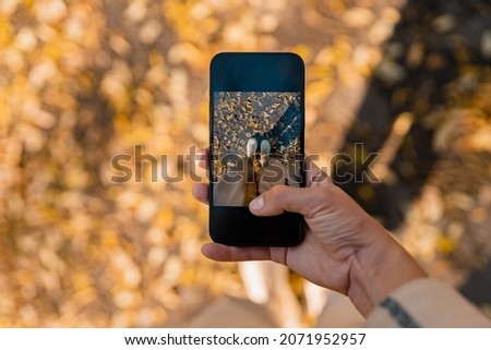 close-up hand of woman walking in autumn park taking pictures of her legs using smartphone fashion style trend