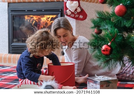 Mother and child with gift at home near Christmas tree and fireplace