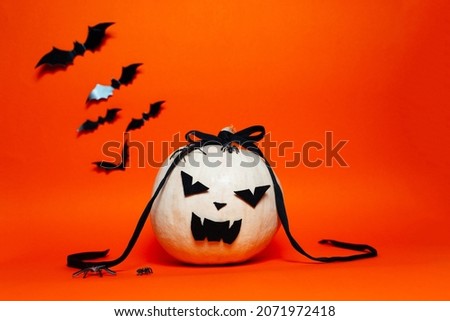 Spooky white pumpkin and buts on orange background.