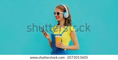 Portrait of smiling young woman in headphones listening to music with smartphone on blue background