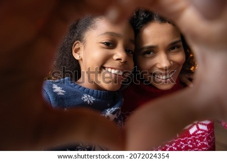 Crop close up of happy young African American mother and teen daughter make heart love hand gesture pose for selfie together. Smiling biracial mom and kid make self-portrait picture on holiday.