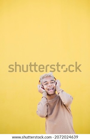 Portrait of Smiling Young man using red headphones and dancing Against yellow Background