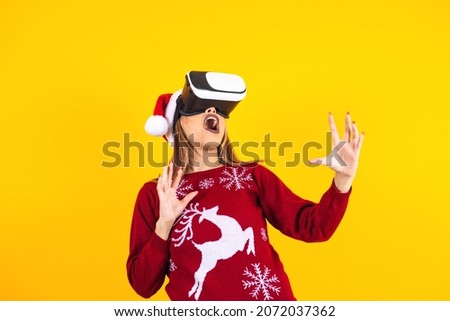 young latin woman gamer in virtual reality headset gadget wearing Santa hat and Christmas sweater on yellow background. Christmas and winter vr technology concept in Mexico Latin America