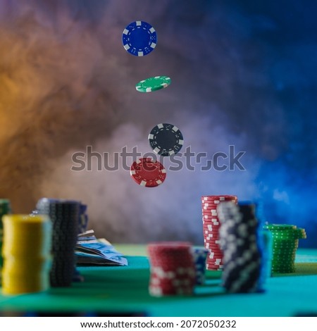 There are stacks of multi-colored chips on the green gambling table. Chips are also in the air. Levitation. Multicolored smoky background. Casino, online casino, gambling, poker, gambling business.