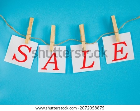 Text sale is written on a white square sheets that is on wooden clothespins on a blue winter background.