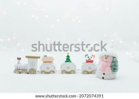 Toy snowman near the wooden white christmas train on the white background with warm lights