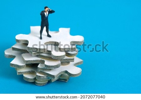 Businessmen standing above jigsaw puzzle piece stack using binoculars. Miniature tiny people toys photography. isolated on blue background.