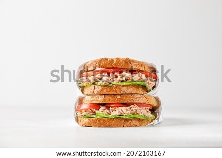 two delicious tuna sandwiches with tomato and cucumber in paper  Royalty-Free Stock Photo #2072103167