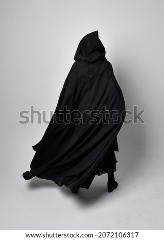 Full length portrait of dark haired girl wearing a witch black flowing gown and  fantasy cloak.   Standing pose with gestural movements, isolated on studio background. Royalty-Free Stock Photo #2072106317