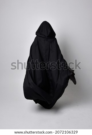 Full length portrait of dark haired girl wearing a witch black flowing gown and  fantasy cloak.   Standing pose with gestural movements, isolated on studio background. Royalty-Free Stock Photo #2072106329