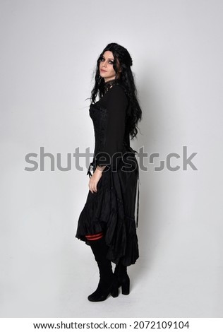 Full length portrait of dark haired girl wearing a fantasy witch black costume.   Standing pose with gestural movements, isolated on studio background.