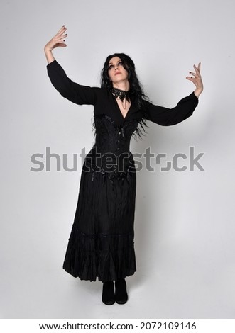 Full length portrait of dark haired girl wearing a fantasy witch black costume.   Standing pose with gestural movements, isolated on studio background.