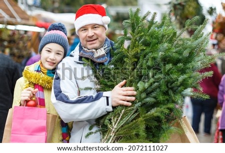 Happy friendly family of father and teen daughter standing on street fair holding fir tree bought for New Year celebration