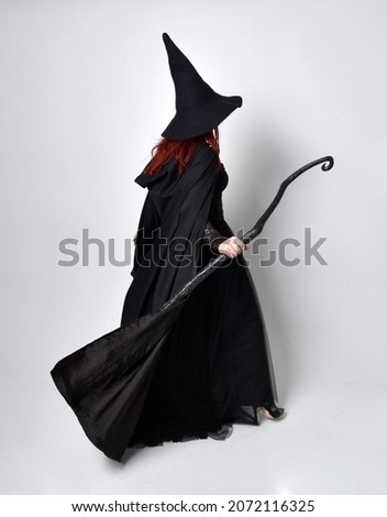 Full length portrait of dark haired girl wearing a fantasy witch black costume.   Standing pose with back to the camera and  gestural movements, isolated on studio background.