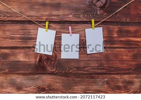 Photo frame made of paper with a clothespin hanging on a rope on a dark wooden background. Mockup for a photo or note