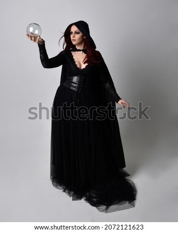 Full length portrait of dark haired girl wearing a fantasy witch black costume and flowing cloak.   Standing pose  gestural movements, isolated on studio background.