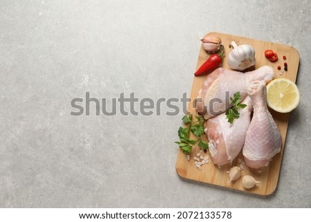 Wooden board with fresh raw chicken legs and other products on light grey table, top view. Space for text