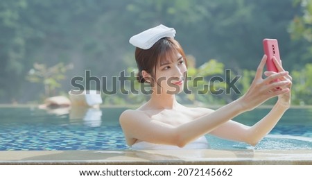 asian young woman putting towel on head take selfie through smart phone while she relaxing sitting in hot spring