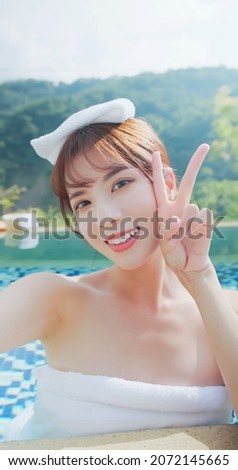 asian young woman putting towel on head take selfie through smart phone while she relaxing sitting in hot spring
