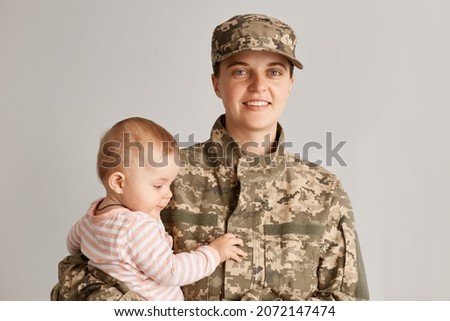 Charming little girl with her military mother, woman soldier holding her daughter, smiling, wearing army uniform, family reunion, motherhood and returning home from war.