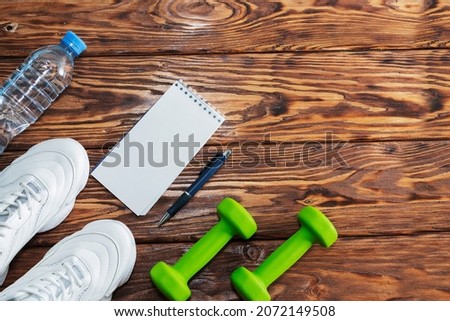 Fitness accessories for women. White athletic shoes, dumbbells, a drinking bottle. An empty space for a motivating, inspiring text. The concept of a healthy lifestyle