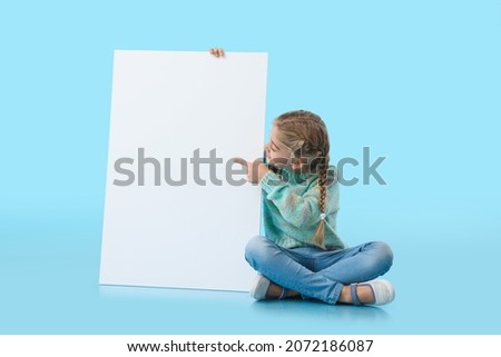 Cute little girl with blank poster on color background