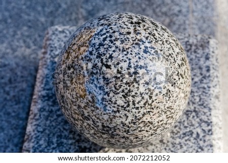 Polished granite ball made with light gray granite as architectural element of the decoration, top view close-up on a blurred background
