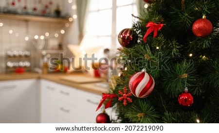 Stylish room interior with beautiful Christmas tree and decorative kitchen in apartment. focus side view on xmas tree full of red balls decor on celebration of holiday with blurred background indoors