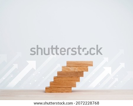 White rise up arrows with wooden blocks arranged as a steps chart on a wooden desk and clean white background with copy space, minimal style. Business growth process and economic improvement concept.