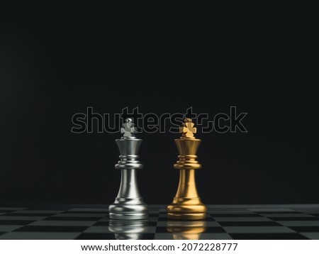 A golden king chess piece and a silver king chess piece are standing together on a chessboard on dark background. Leadership, partnership, competitor, confrontation, and business strategy concept. Royalty-Free Stock Photo #2072228777