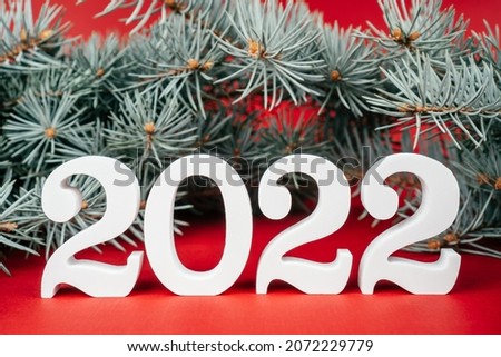 Happy New Year 2022. White wooden numbers 2022 stand with lush green Christmas tree branches on red background. Merry Christmas.