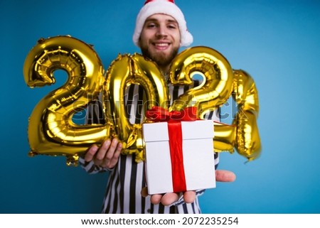 A man in a Christmas hat holds the numbers 2022 and a gift box. Selective focus on the box