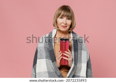 Smiling blithesome charismatic vivid fun mature elderly senior lady woman 55 years old wears motley plaid hold thermos trying to warm up isolated on plain pastel light pink background studio portrait Royalty-Free Stock Photo #2072235893