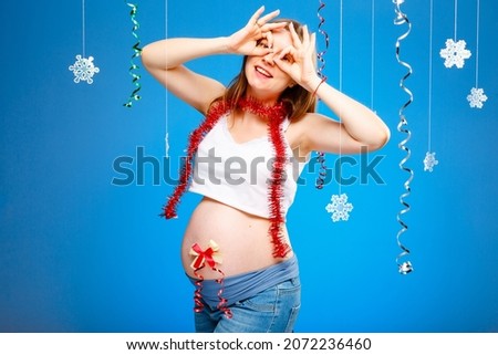 Pregnant woman with snowflakes on a blue background and red garland, the concept of expecting a baby on Christmas eve. New year baby birth.