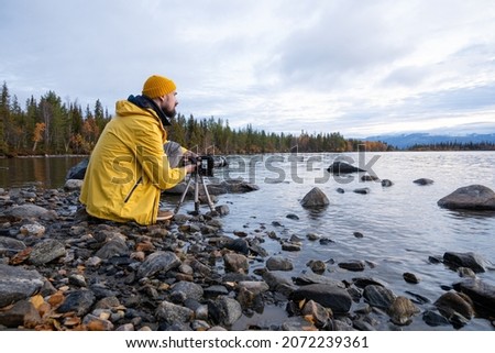 Professional nature photographer taking photo of lake wearing bright yellow coat