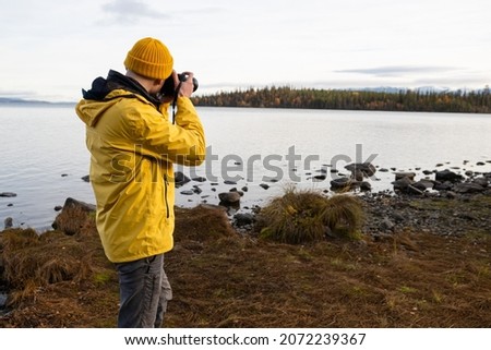 Professional nature photographer taking photo of lake wearing bright yellow coat