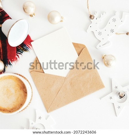 Christmas composition. Craft paper envelope with blank paper card mockup, scarf, coffee cup, vintage Christmas decoration on white table. Flat lay, top view, copy space.