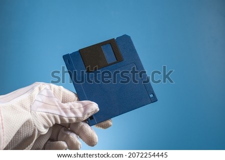Blank floppy disc of blue color in hand, on a blue background. Outdated retro digital media. Old computer technology.